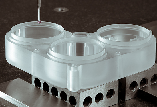 Machined frosted acrylic component held in a vice while being measured