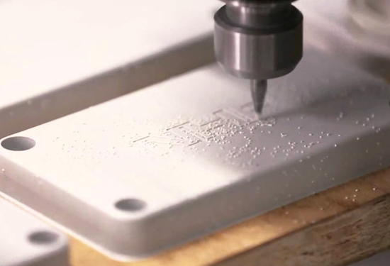 CNC router bit engraving detail into a white plastic panel